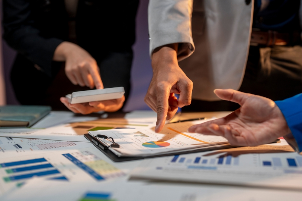Three,People,Are,Looking,At,A,Table,With,A,Lot